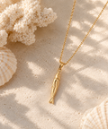 Gold-tone fish pendant necklace on a sandy backdrop