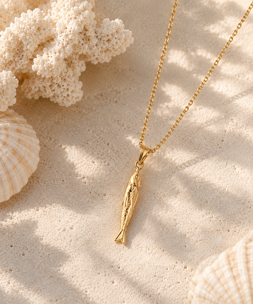 Gold-tone fish pendant necklace on a sandy backdrop